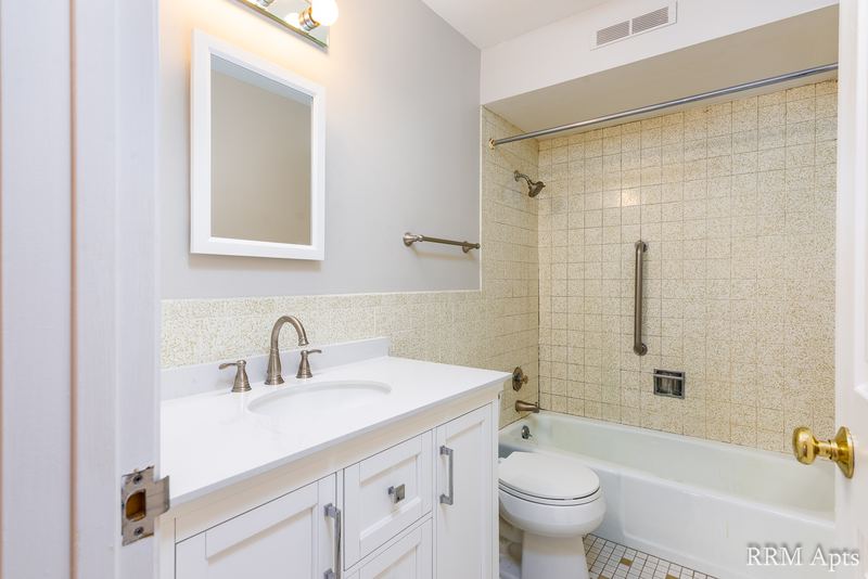 Bathroom with beige tile tub surround, white vanity, mirrored medicine cabinet and grab bar, Maple Avenue apartment 1H