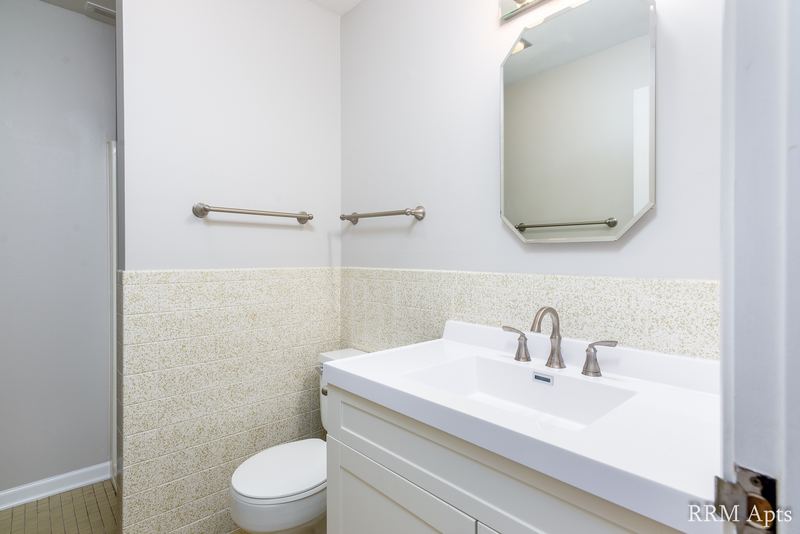 Bathroom with white vanity, mirrored medicine cabinet, beige tile wainscot and towel bars, Maple Avenue apartment 1H
