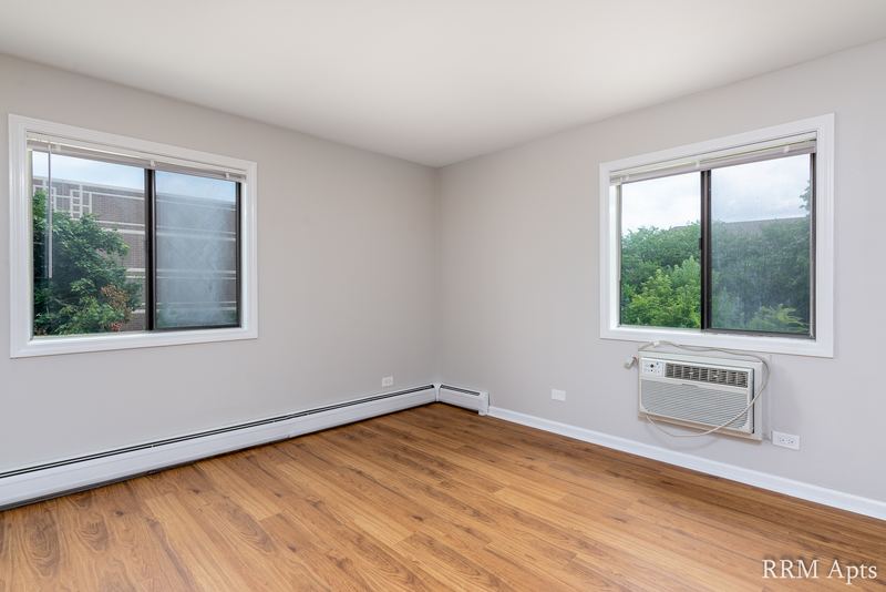 Bedroom with wood laminate floor, two windows with trees outside and a wall air conditioner, Maple Avenue apartment 1H