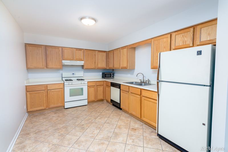 Kitchen with wood cabinets, white stove, dishwasher and refrigerator, and beige tile floor, Maple Avenue apartment 1J