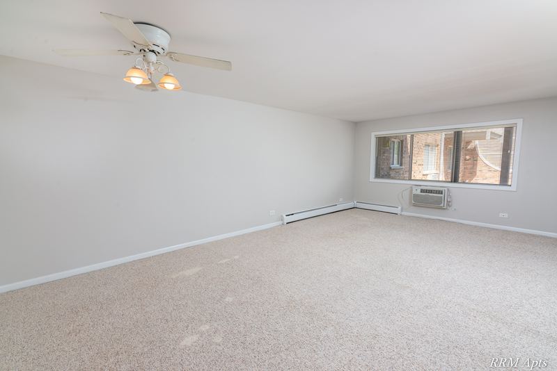Living room with beige carpet, ceiling fan, a window with wall air conditioner and baseboard heat, Maple Avenue apartment 1J