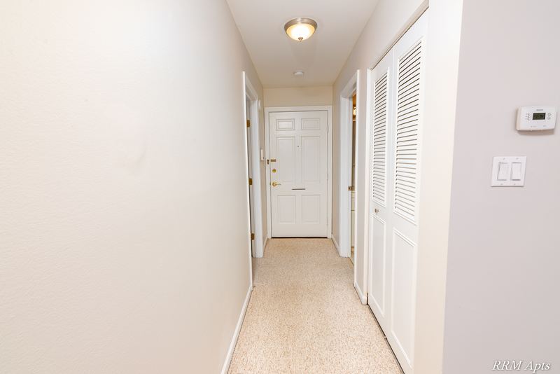Hallway with white louvered closet doors, the entry door and a thermostat on the wall, Maple Avenue apartment 1J