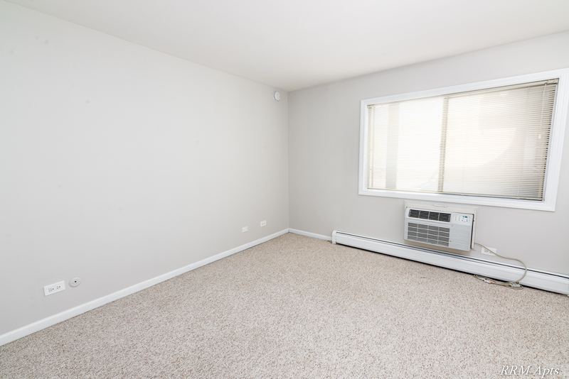Bedroom with beige carpet, a window with wall air conditioner and baseboard heat, Maple Avenue apartment 1J