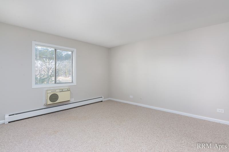 Bedroom with beige carpet, a window with trees outside, wall air conditioner and baseboard heat, Maple Avenue apartment 2A