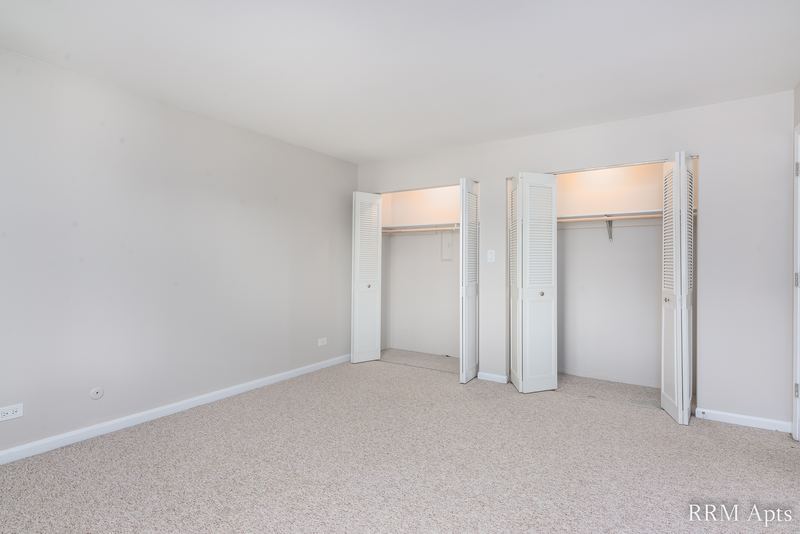 Bedroom with beige carpet, gray walls and two open closets with white bifold doors, Maple Avenue apartment 2A