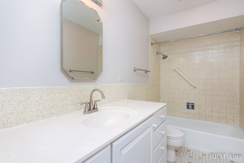 Bathroom with white vanity, arched mirror, beige tile tub surround and grab bar, Maple Avenue apartment 2A