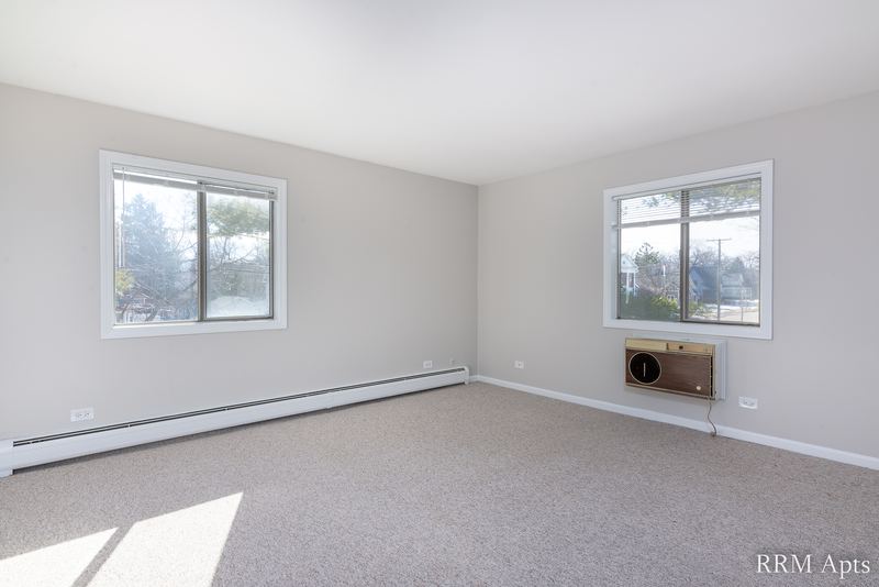 Bedroom with beige carpet, two windows with trees outside, wall air conditioner and baseboard heat, Maple Avenue apartment 2A