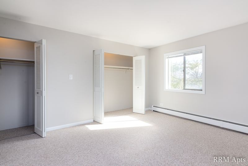 Bedroom with beige carpet, two open closets with louvered doors and a window with baseboard heat, Maple Avenue apartment 2A