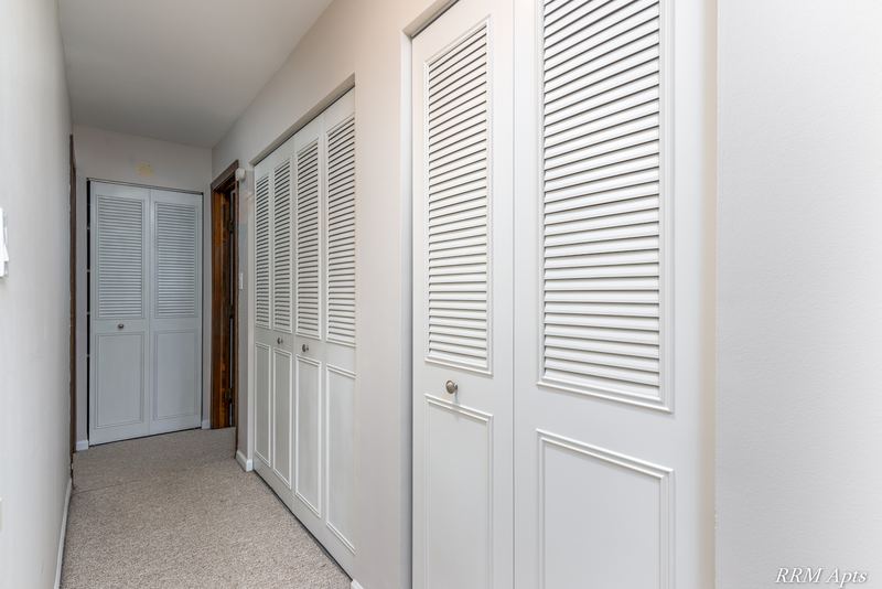 Hallway with white louvered closet doors and a white door at the end, Maple Avenue apartment 2C