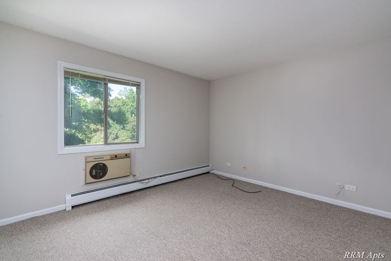 Bedroom with beige carpet, a window with trees outside, wall air conditioner and baseboard heat, Maple Avenue apartment 2C