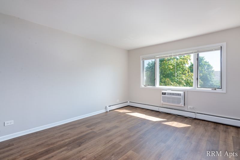 Living room with wood laminate floor, a window with trees outside and a wall air conditioner, Maple Avenue apartment 2F