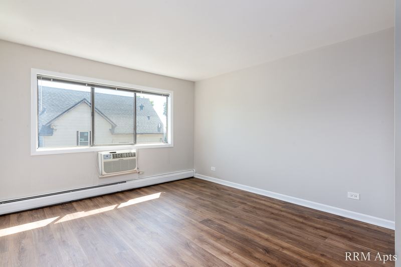 Bedroom with wood laminate floor and a window with wall air conditioner looking out on houses, Maple Avenue apartment 2F