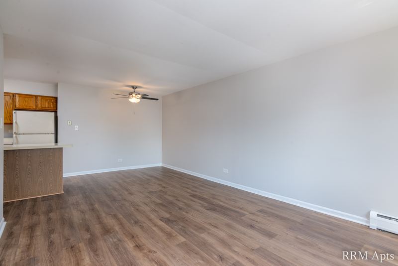 Living room with wood laminate floor, ceiling fan and kitchen peninsula with white refrigerator, Maple Avenue apartment 2F
