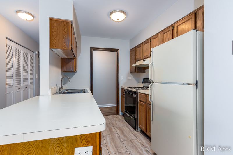 Kitchen with wood cabinets, white refrigerator, black stove, peninsula and laminate floor, Maple Avenue apartment 2F