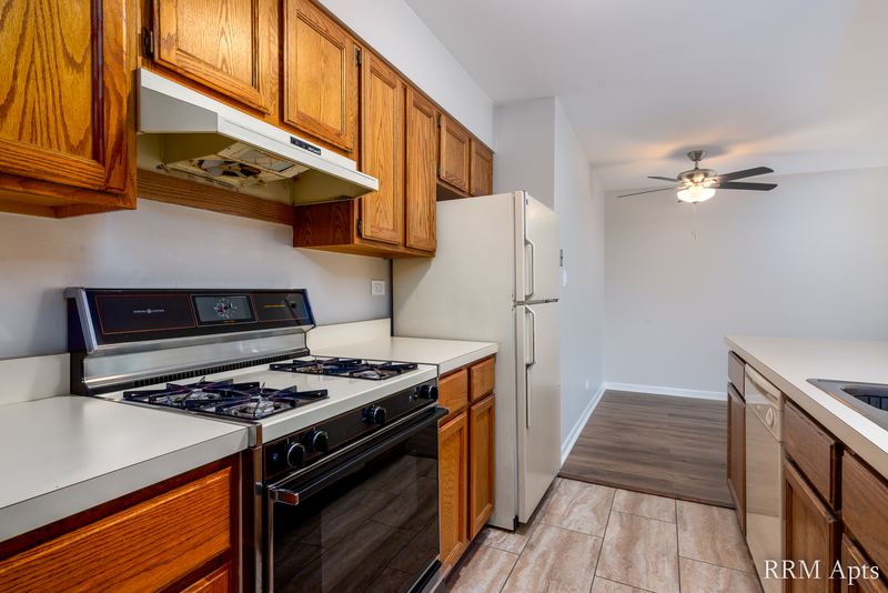 Kitchen with wood cabinets, black gas stove under a range hood and white refrigerator, Maple Avenue apartment 2F
