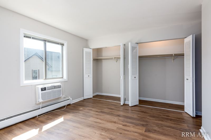 Bedroom with wood laminate floor, a window with wall air conditioner and two open closets, Maple Avenue apartment 2F