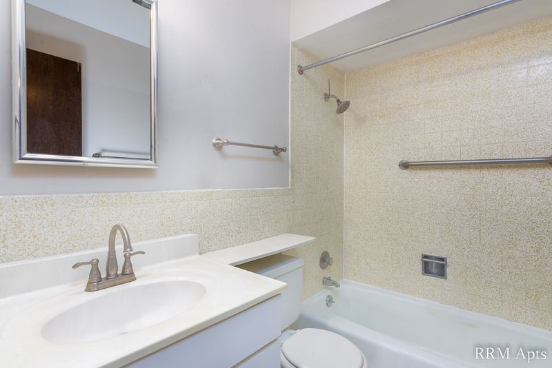 Bathroom with beige tile tub surround, white vanity, mirrored medicine cabinet and towel bar, Maple Avenue apartment 2F
