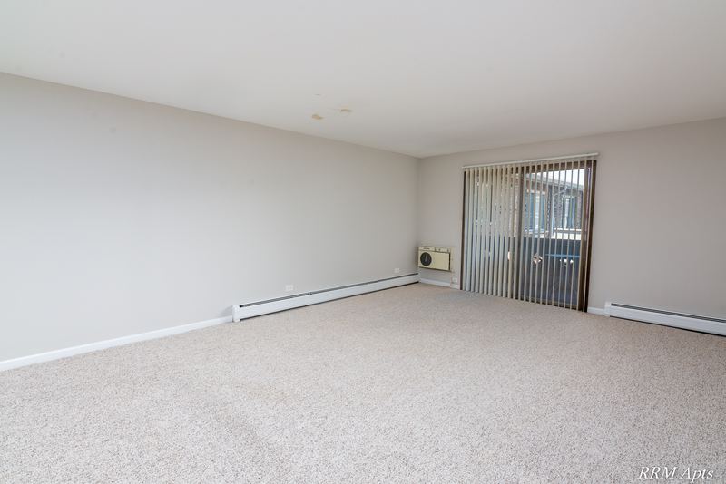 Living room with beige carpet, a window with vertical blinds and a wall air conditioner, Maple Avenue apartment 2J