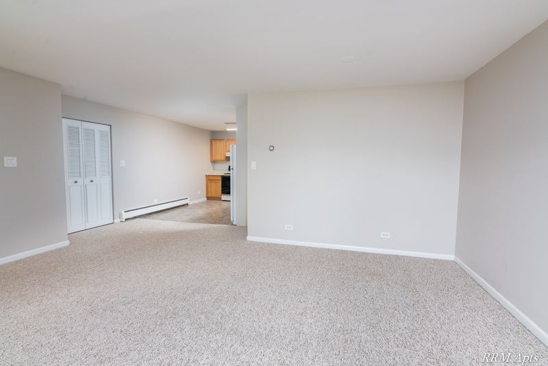 Living room with beige carpet, white louvered closet doors and a view through to the kitchen, Maple Avenue apartment 2J