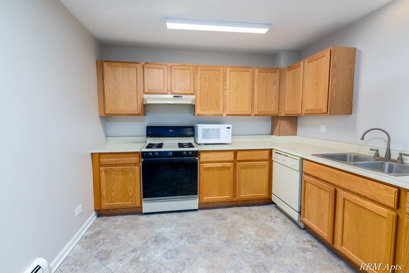 Kitchen with wood cabinets, white stove under a range hood, microwave and stainless sink, Maple Avenue apartment 2J