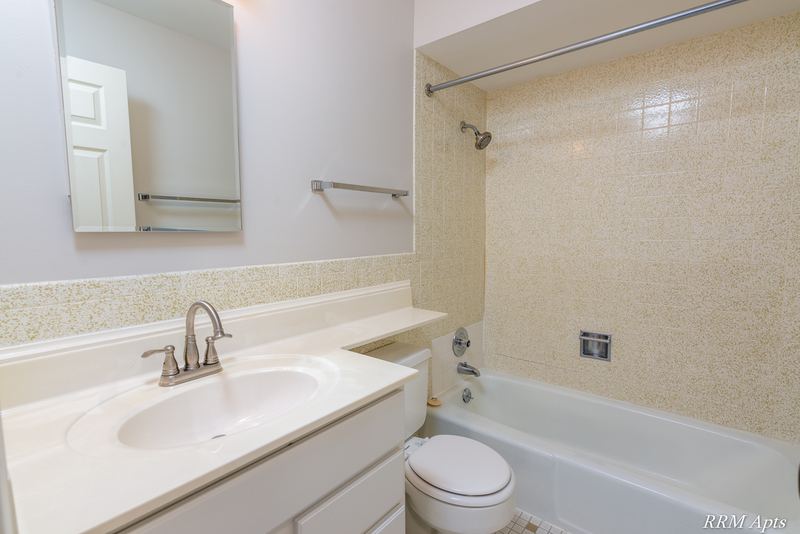 Bathroom with beige tile tub surround, white vanity, mirrored medicine cabinet and towel bar, Maple Avenue apartment 2J