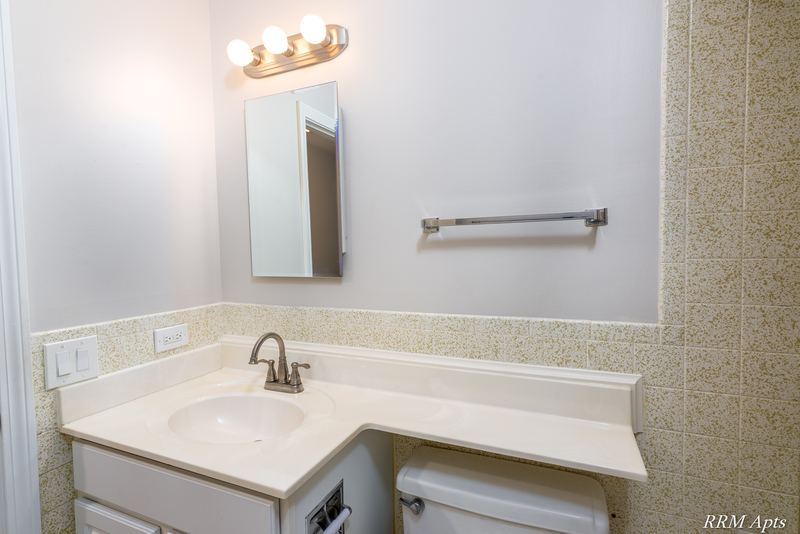 Bathroom with white vanity, mirror with strip light, beige tile wainscot and towel bar, Maple Avenue apartment 2J