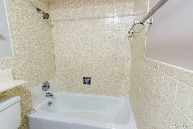 Bathroom with white tub, beige tile surround, grab bar and toilet, Maple Avenue apartment 2J