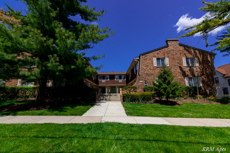 Two-story brick apartment building with front walkway, lawn and mature pine trees at Maple Avenue, Libertyville