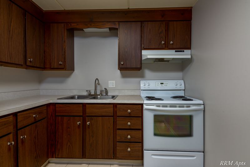 Kitchen with dark wood cabinets, stainless sink and white electric stove under a range hood, Maple Avenue apartment LL1