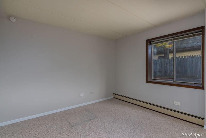 Bedroom with beige carpet, a window looking out on a wood fence and baseboard heat, Maple Avenue apartment LL1
