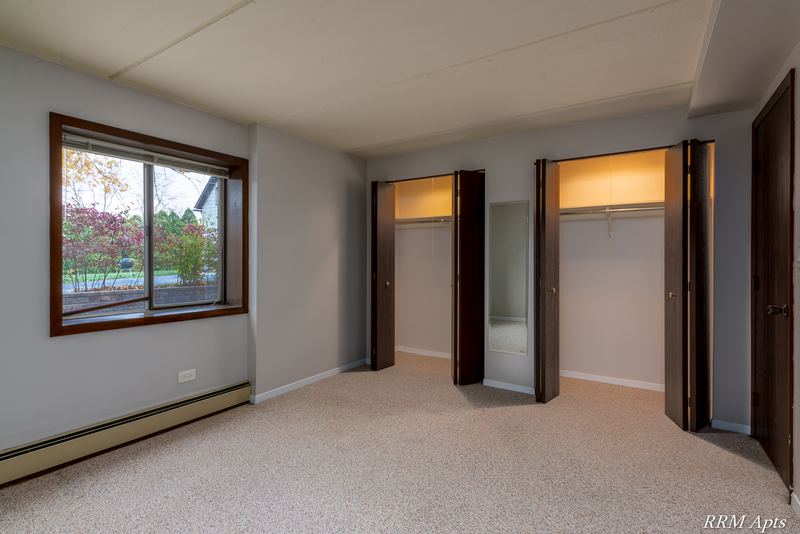 Bedroom with beige carpet, a window with trees outside, two open closets and baseboard heat, Maple Avenue apartment LL1