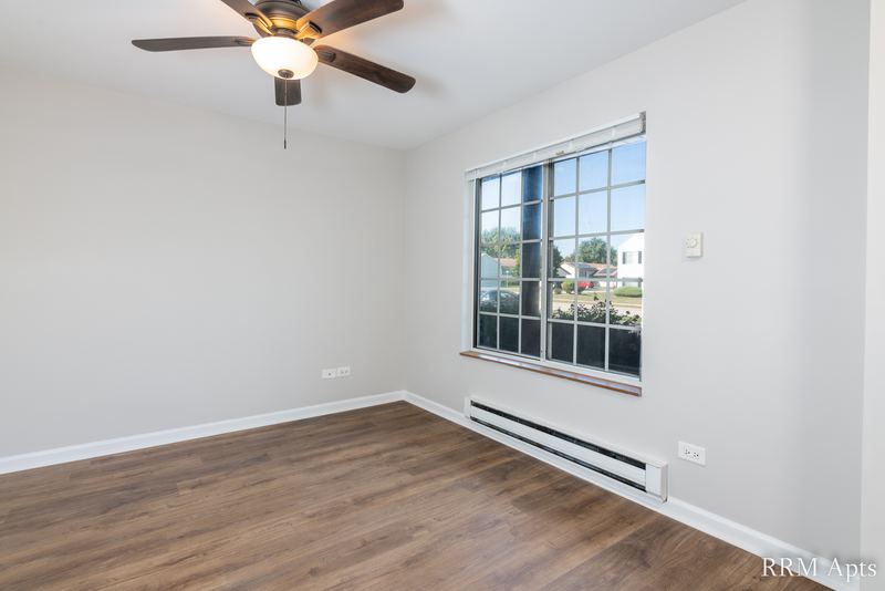Living room with wood laminate floor, ceiling fan, a grid-pane window and baseboard heat, Oriole Court apartment 1B