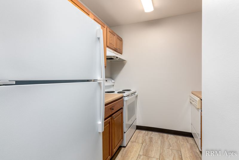 Kitchen with white refrigerator, wood cabinets, white stove and dishwasher, and laminate floor, Oriole Court apartment 1B