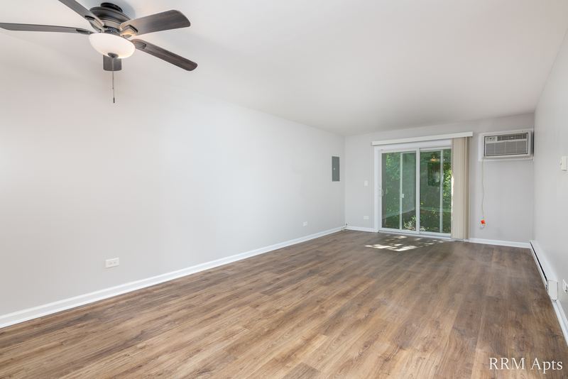 Living room with wood laminate floor, ceiling fan, sliding glass door and a wall air conditioner, Oriole Court apartment 1B