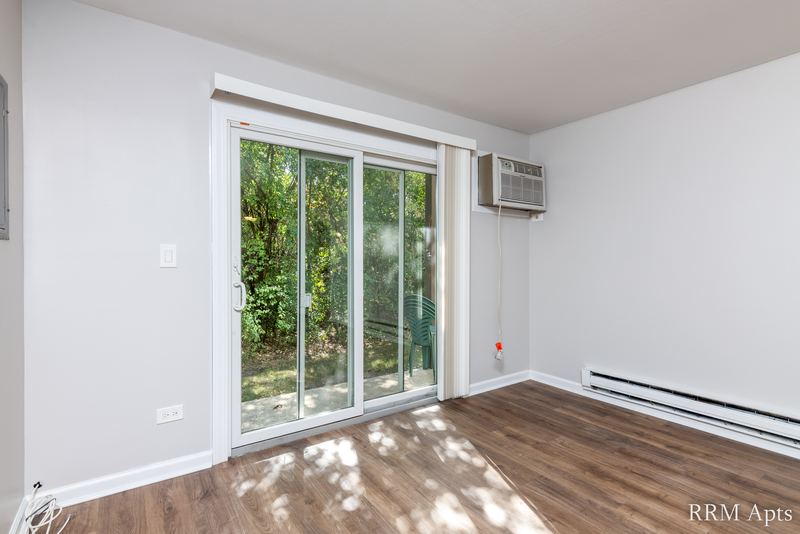 Living room with wood laminate floor, sliding glass door to trees and a wall air conditioner, Oriole Court apartment 1B