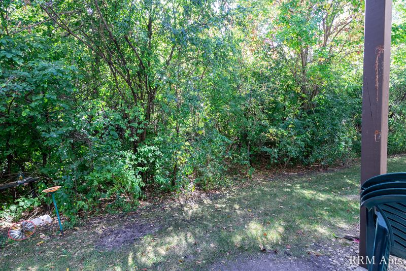 Patio view with a wood post, lawn and dense green trees outside the sliding door, Oriole Court apartment 1B