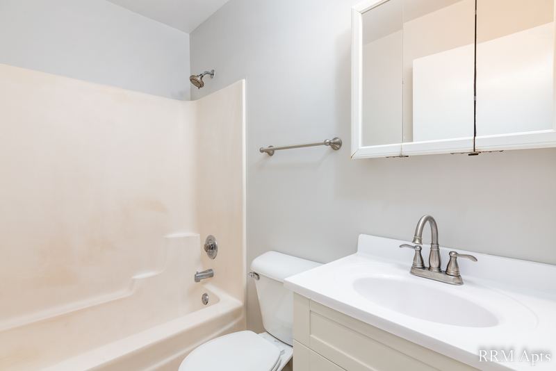Bathroom with white tub surround, white vanity, mirrored medicine cabinet and toilet, Oriole Court apartment 1B