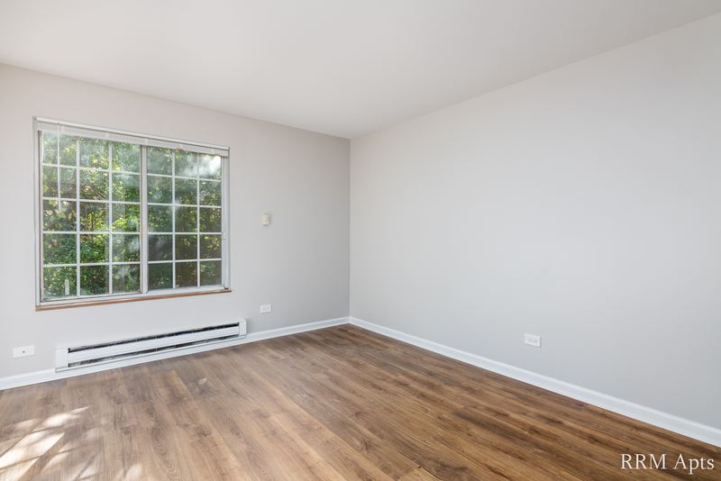 Bedroom with wood laminate floor, a grid-pane window with trees outside and baseboard heat, Oriole Court apartment 1B