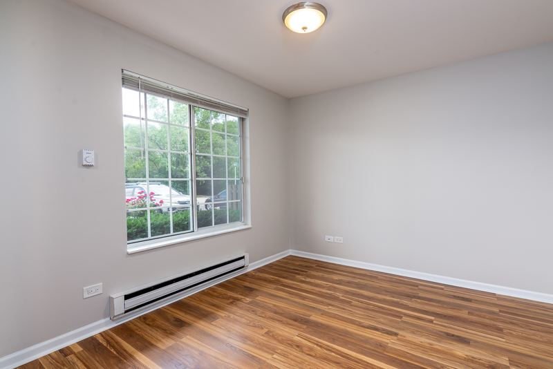 Bedroom with wood laminate floor, a grid-pane window looking out on parked cars and baseboard heat, Oriole Court apartment 1C