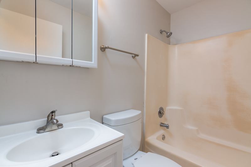 Bathroom with white vanity, mirrored medicine cabinet, white tub surround and toilet, Oriole Court apartment 1C