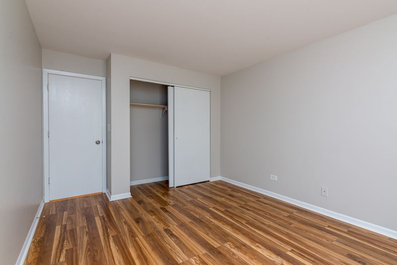 Bedroom with wood laminate floor, an open closet with wood bifold door and a white door, Oriole Court apartment 1C