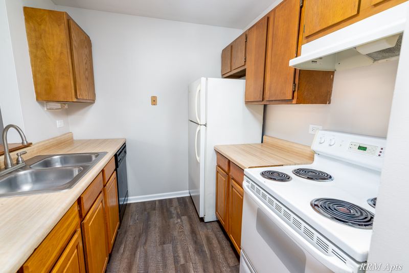 Kitchen with wood cabinets, white electric stove under a range hood and black dishwasher, Oriole Court apartment 2A