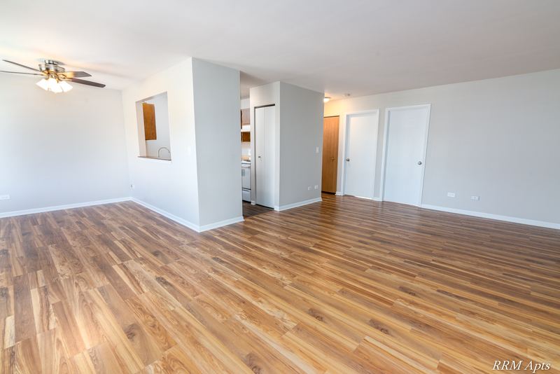 Living room with wood laminate floor, ceiling fan and a hallway with white doors beyond, Oriole Court apartment 2A