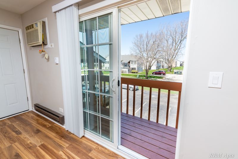 Balcony with wood railing seen through the sliding glass door, wall air conditioner above, Oriole Court apartment 2A