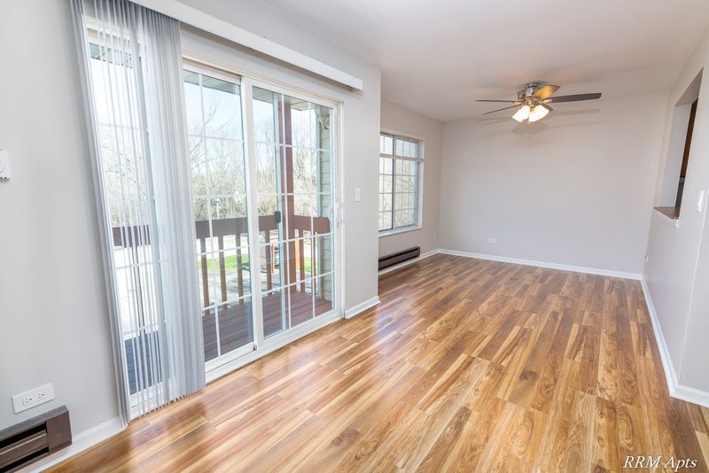 Living room with wood laminate floor, ceiling fan and sliding door to a wood-railed balcony, Oriole Court apartment 2A
