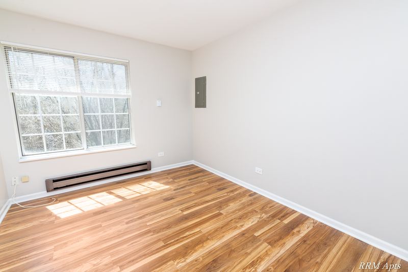 Bedroom with wood laminate floor, a grid-pane window looking out on trees and a wall vent, Oriole Court apartment 2A