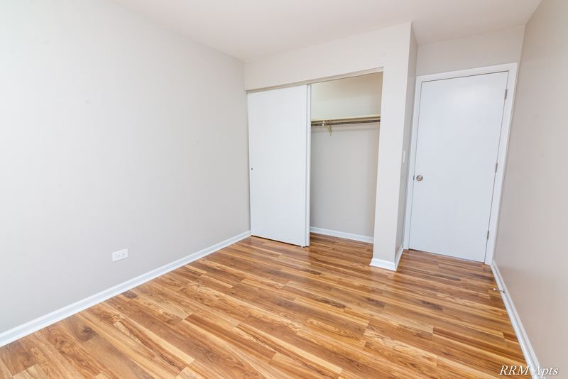 Bedroom with wood laminate floor, an open closet with shelf and rod, and a white door, Oriole Court apartment 2A