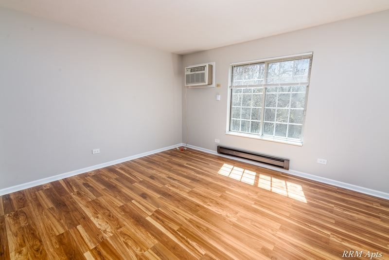 Bedroom with wood laminate floor, a grid-pane window, wall air conditioner and baseboard heat, Oriole Court apartment 2A