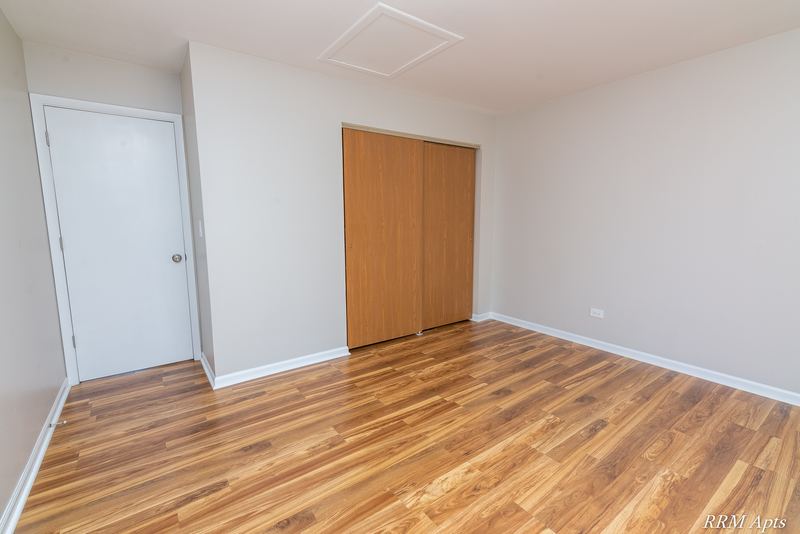 Bedroom with wood laminate floor, a white door and closed wood bifold closet doors, Oriole Court apartment 2A