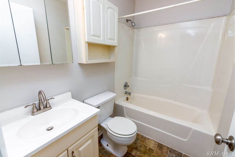 Bathroom with white vanity, mirrored medicine cabinet, white wall cabinet and white tub surround, Oriole Court apartment 2A